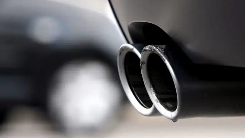Close-up of twin chrome exhaust pipes on a dark vehicle undercarriage, highlighting vehicle emission output